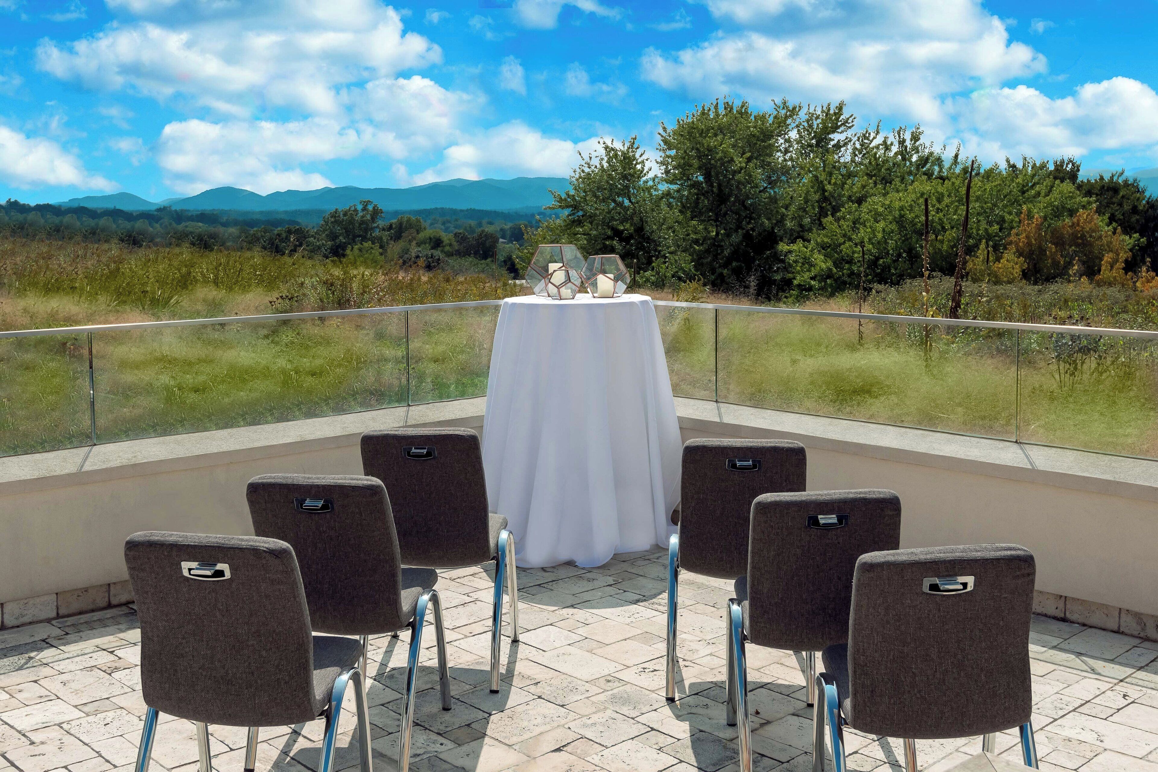 A terrace with a table set for six, overlooking a scenic landscape with mountains and trees.