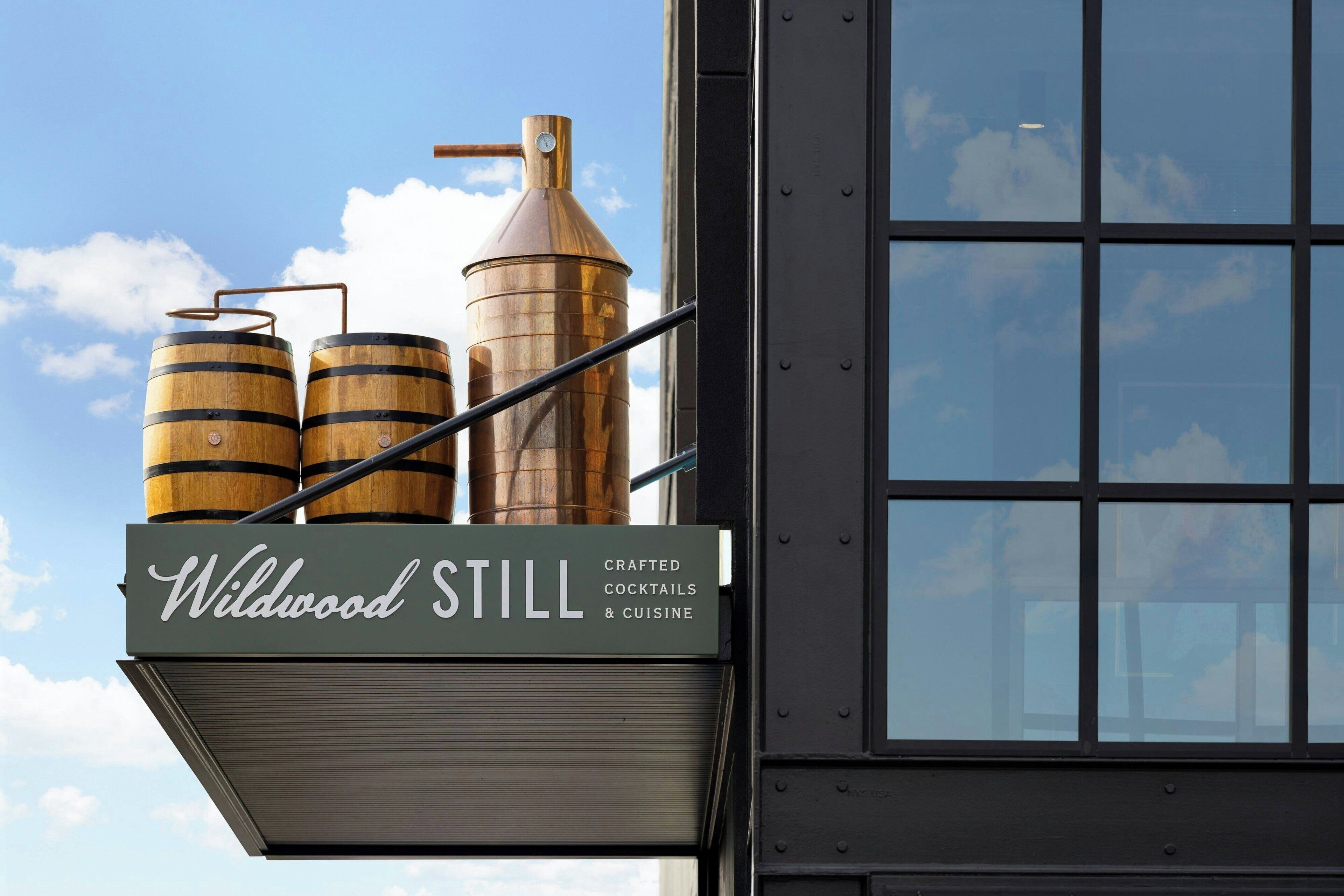A building with a sign that reads "Wildwood Still" and features two wooden barrels and a copper still.