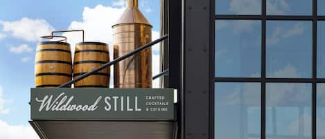 A building with a sign that reads "Wildwood Still" and features two wooden barrels and a copper still.