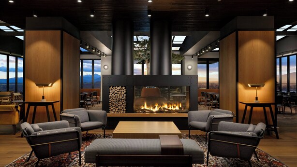 A modern lounge area with a central fireplace, comfortable seating, and large windows offering a view of the outdoors. - Aloft by Marriott Asheville Downtown (Asheville)