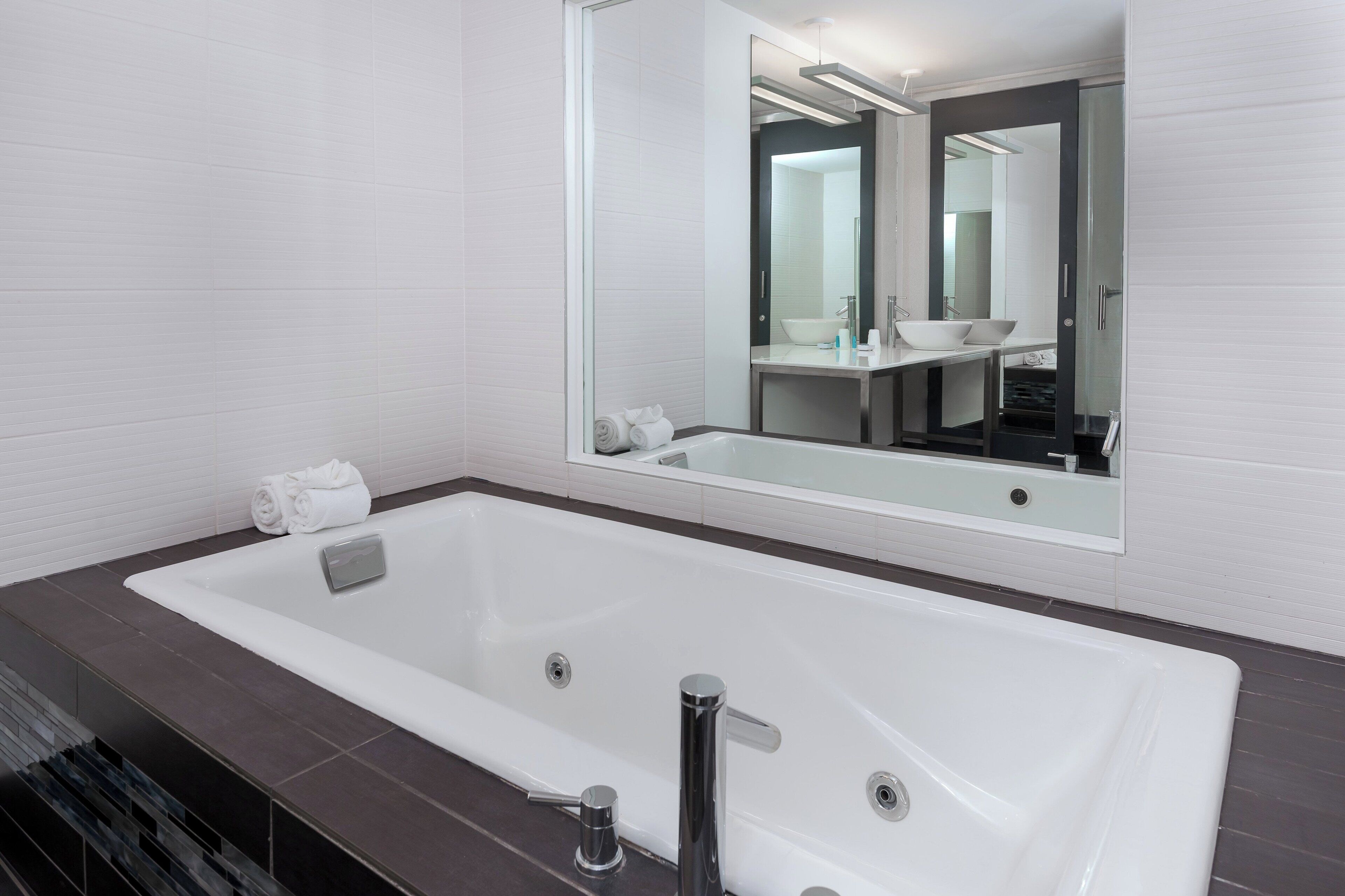 Un baño moderno con una bañera grande, un espejo y un lavabo.