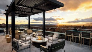 A rooftop terrace with outdoor seating, a fire pit, and a view of the cityscape and mountains. - Aloft by Marriott Asheville Downtown (Asheville)