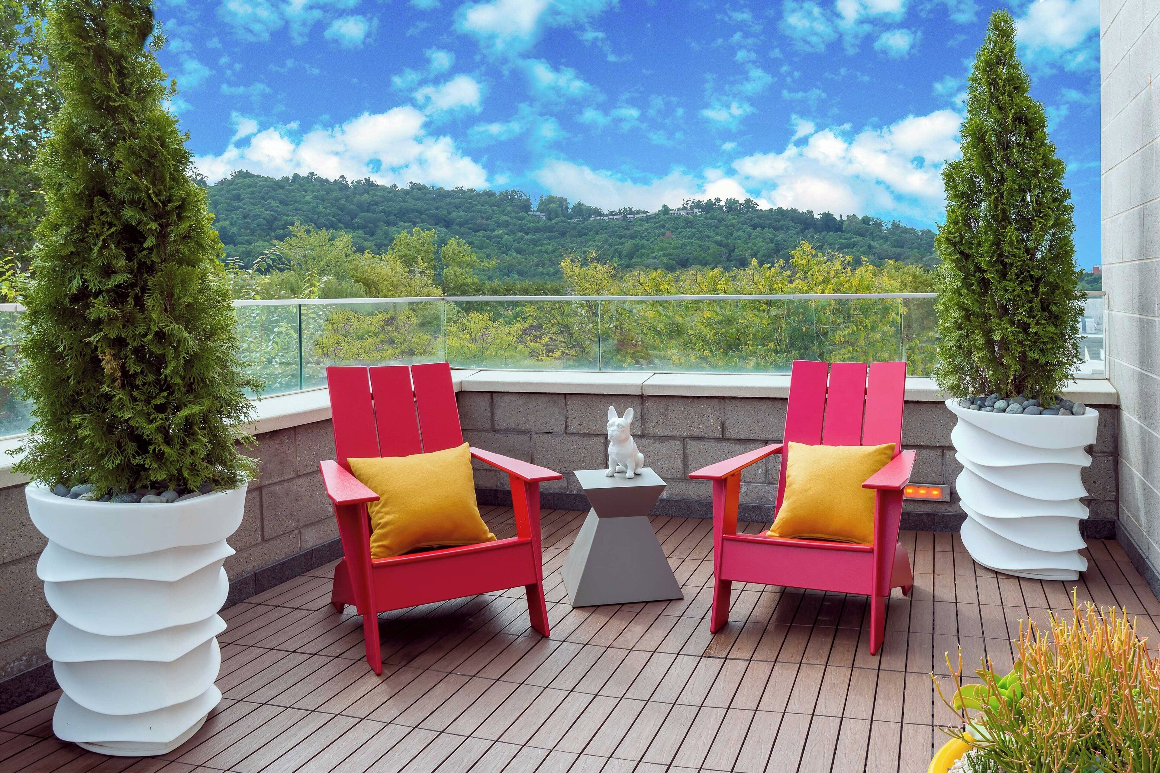 A balcony with two red chairs, a small table, and two large potted plants.