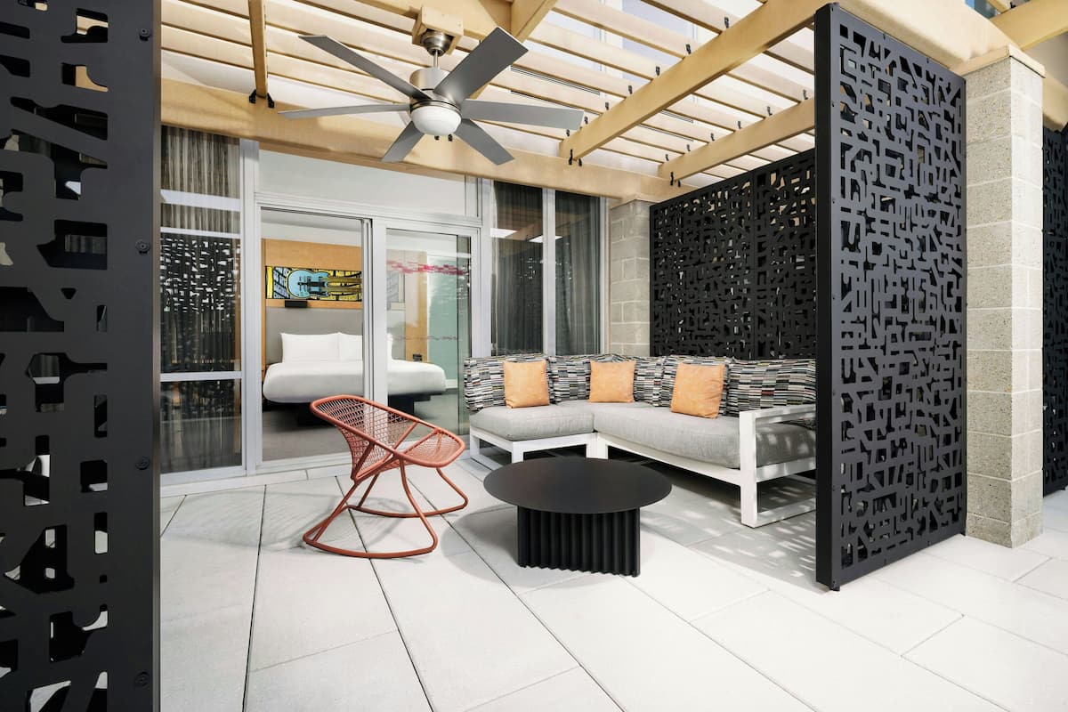 A modern outdoor seating area with a sofa, a round black table, and a red chair.