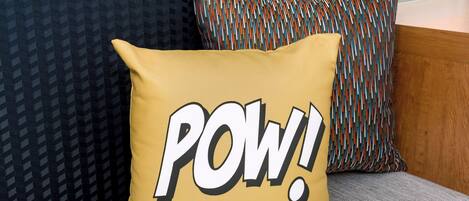 A sofa with a mustard-colored pillow featuring bold text and a multicolored pillow.