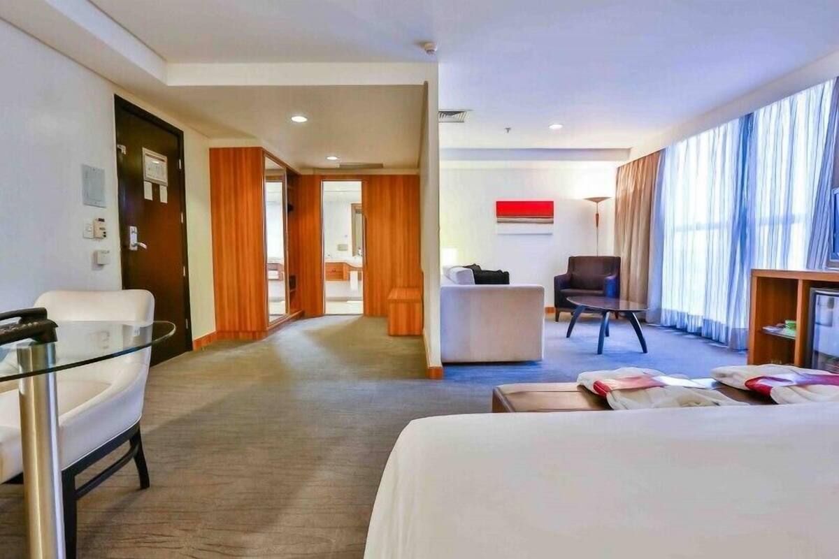 Una habitación de hotel con cama, una mesita de vidrio, una silla, un sofá y un escritorio.