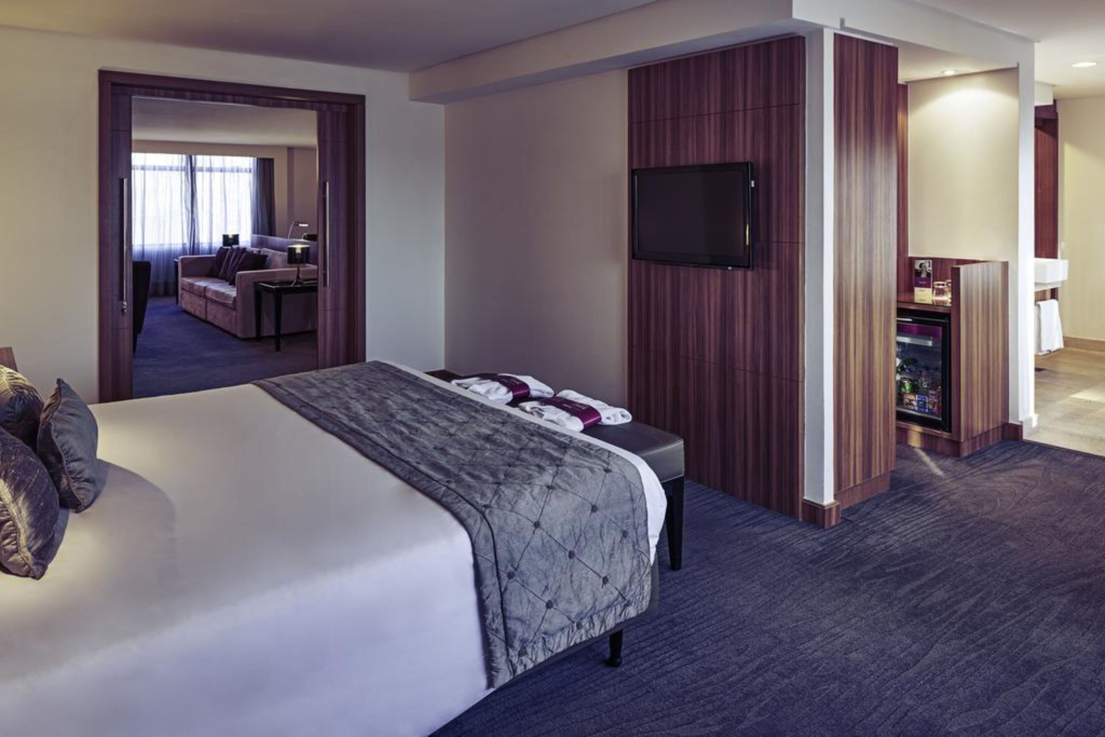 Una habitación de hotel con una cama grande, un televisor montado en la pared y un escritorio con una computadora.