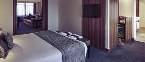 Una habitación de hotel con una cama grande, un televisor montado en la pared y un escritorio con una computadora.