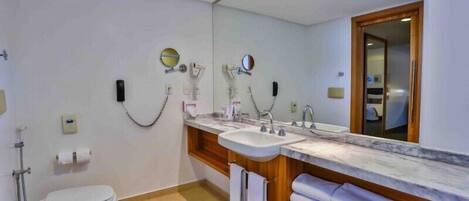 Un baño moderno con inodoro, dos lavamanos, un espejo grande y ducha.