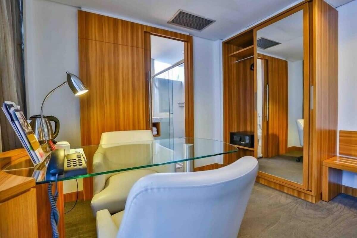 Una oficina moderna con escritorio de vidrio, silla de cuero blanco, paneles de madera y un espejo grande.