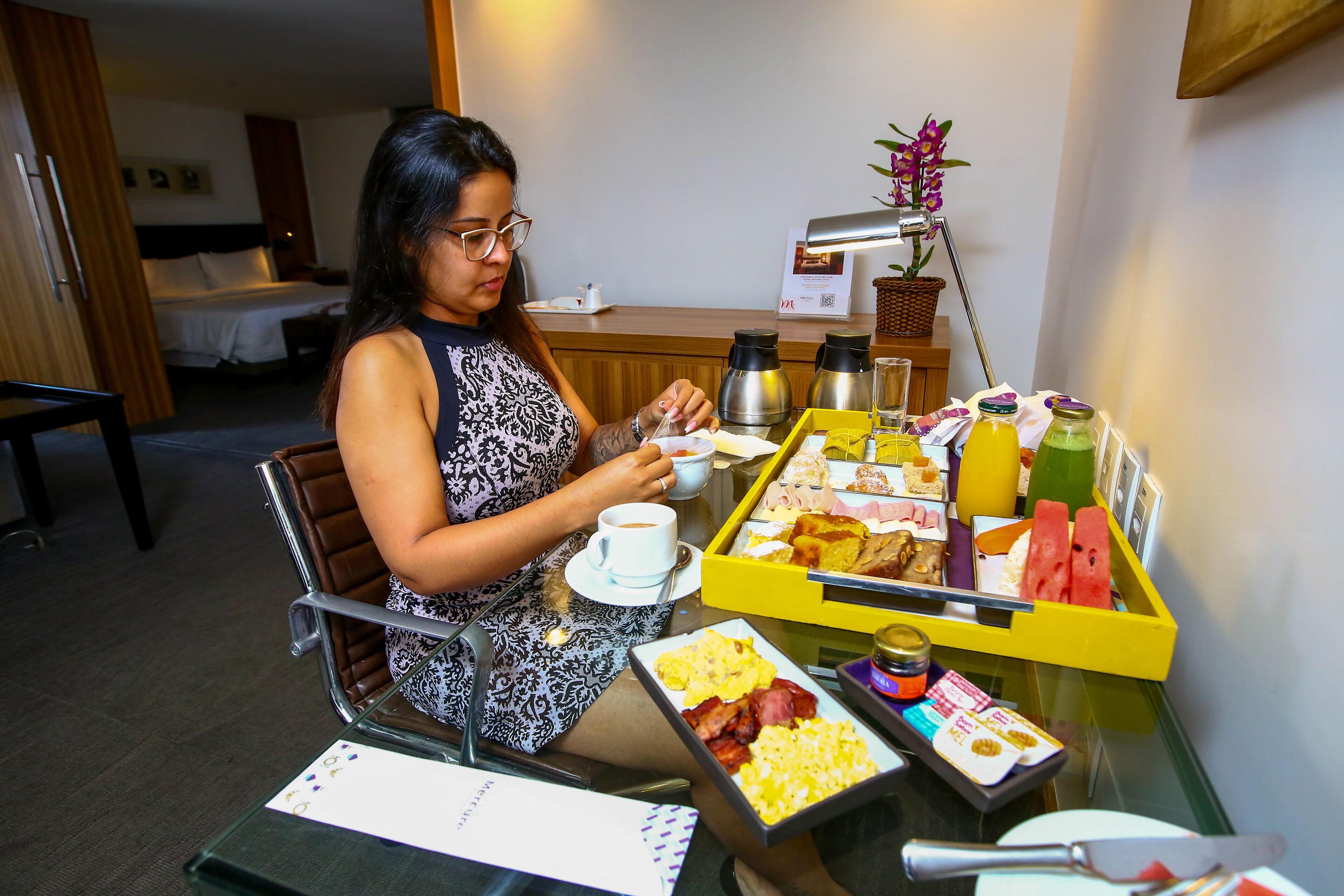 A hotel room with a dining table set for breakfast, including various food items and beverages.