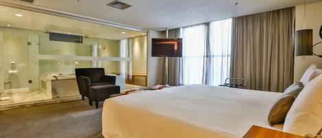 A hotel room with a large bed, a TV, a desk, and a glass-enclosed shower area.