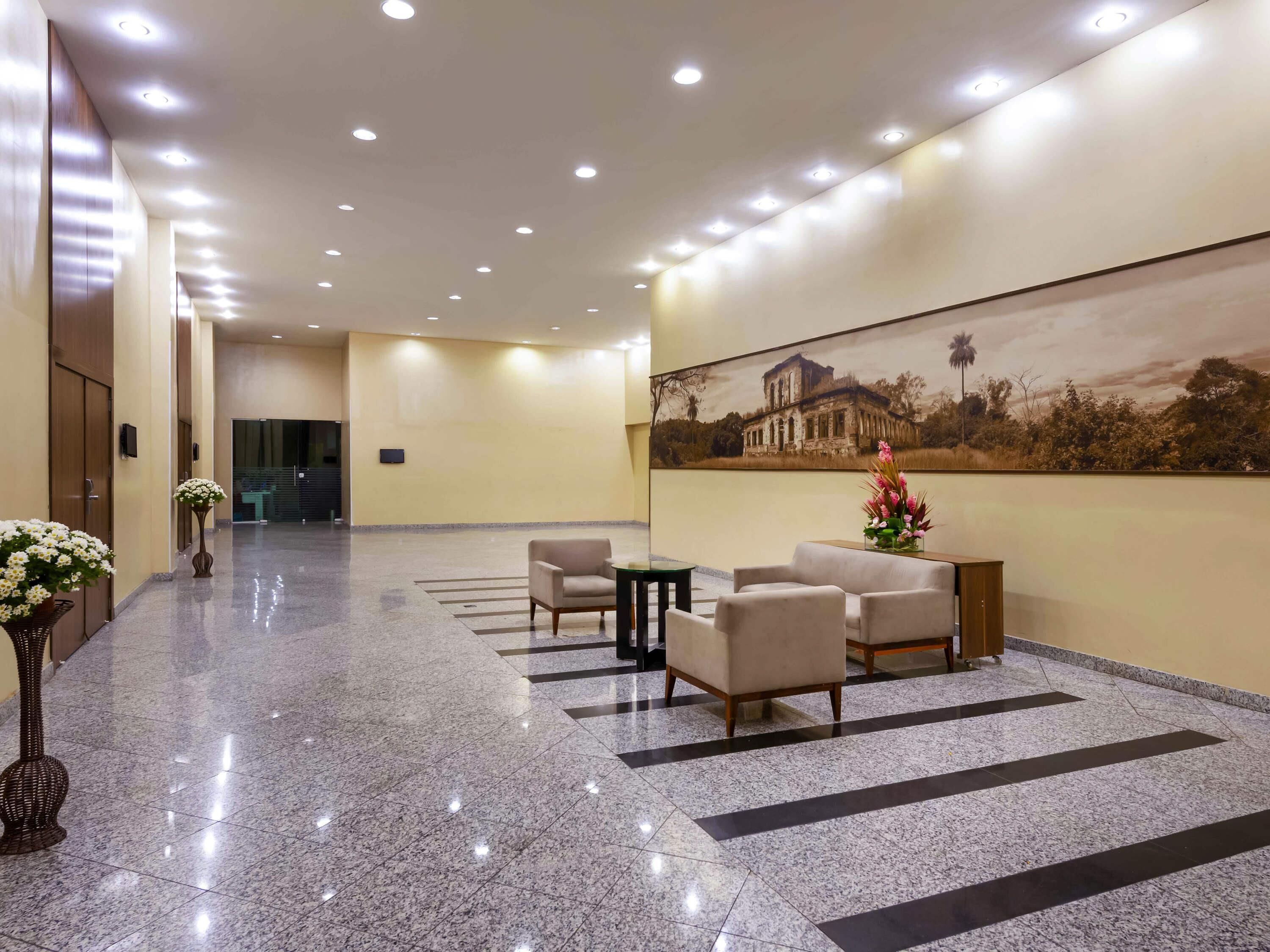 Un hall d’hôtel doté d’un sol en marbre poli, d’un espace salon avec des fauteuils et une petite table, d’un grand tableau accroché au mur et d’un comptoir de réception.