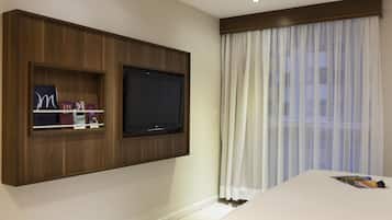 A hotel room with a mounted TV, a bed, and a window with sheer curtains.