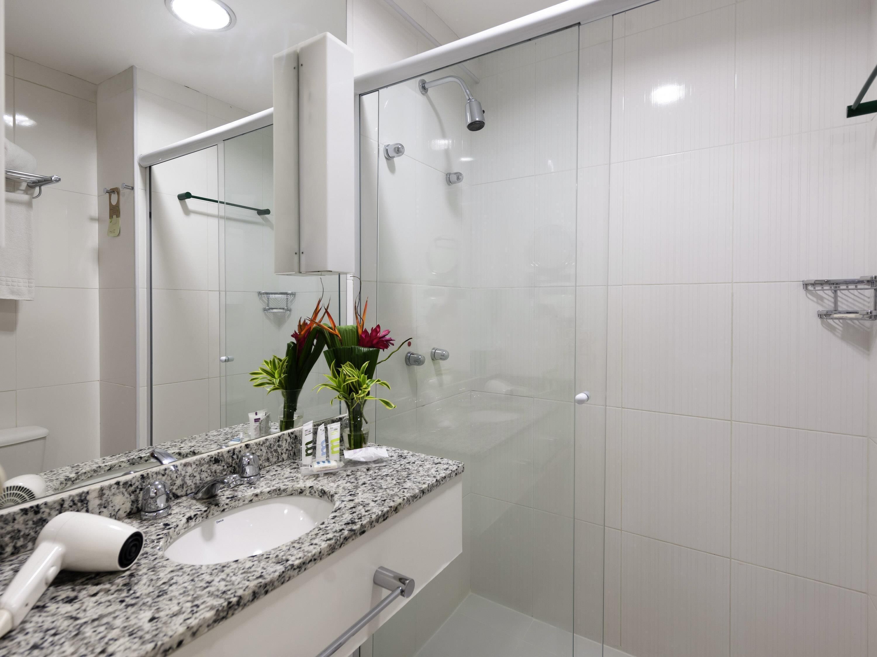 A modern bathroom with a granite countertop, a glass shower enclosure, and a large mirror.