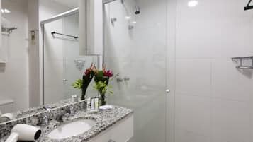 A modern bathroom with a granite countertop, a glass shower enclosure, and a large mirror.