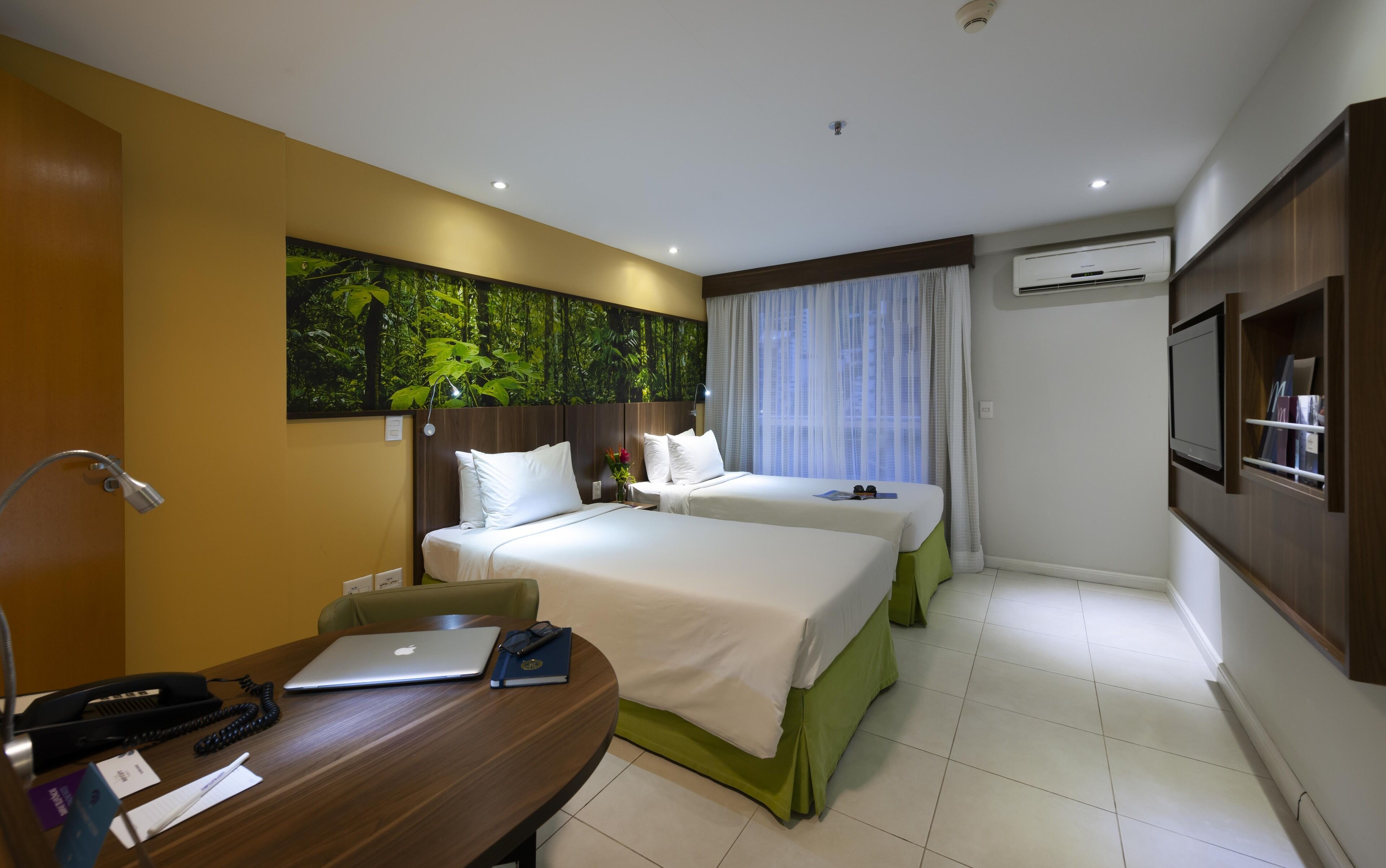 Habitación de hotel con dos camas, un escritorio, una computadora portátil, un teléfono y un televisor.