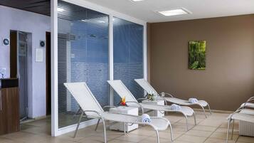 Um quarto com poltronas de vime branco, um painel de vidro, uma parede marrom com uma obra de arte verde e um chão de azulejos.