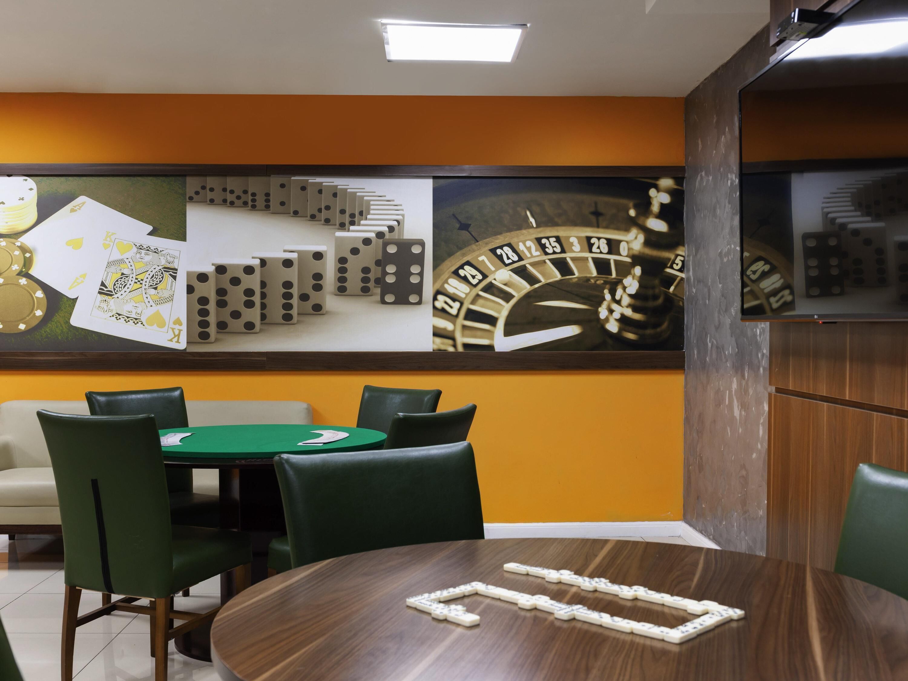 Une pièce avec une table verte, quatre chaises, une horloge et un mur décoré de dominos et de jeux de cartes.