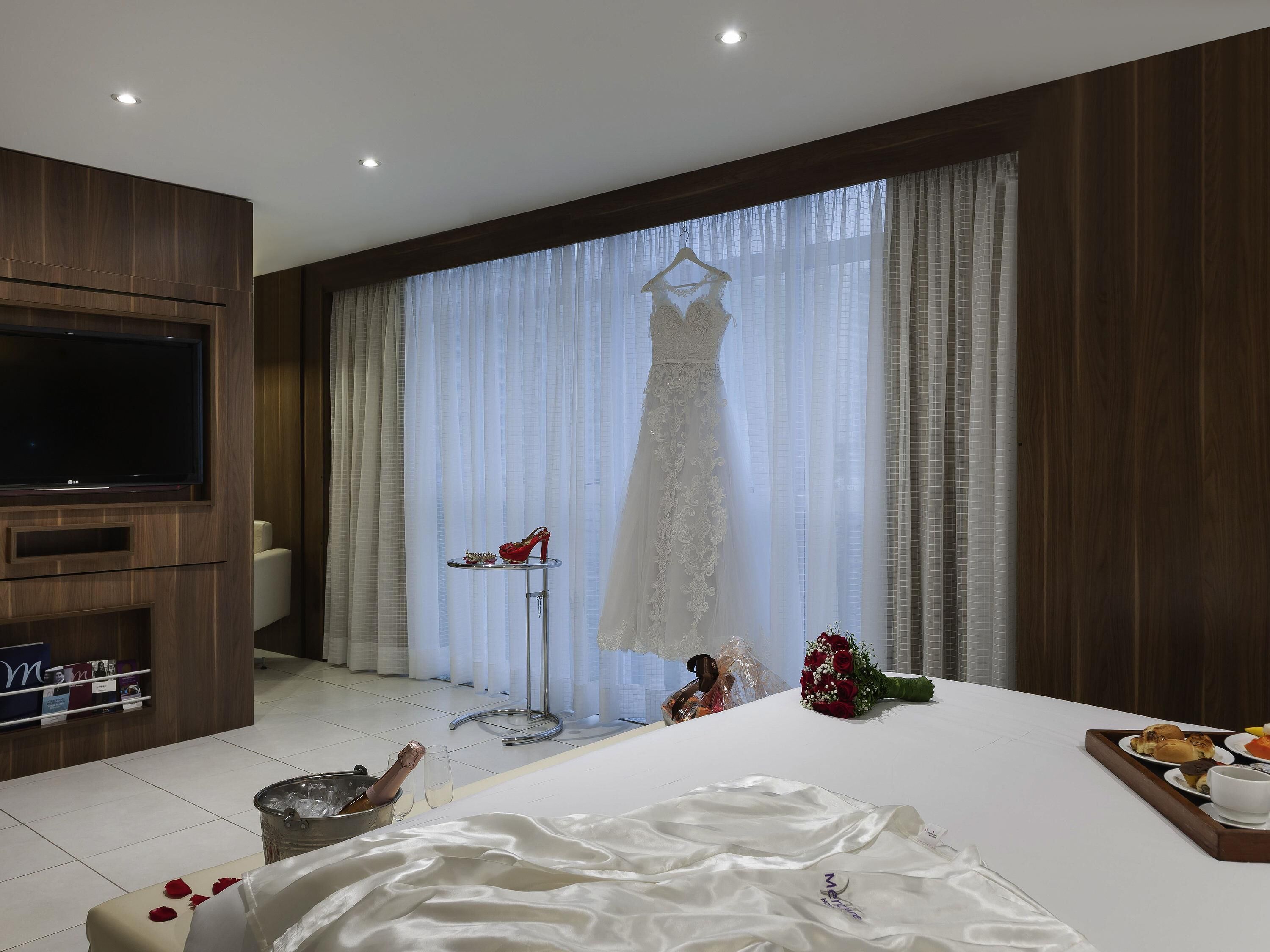 A hotel room with a bed, a TV, a window with curtains, and a table with a tray of food.