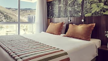 A hotel room with a large bed, two pillows, a view of the city, and a forest mural on the wall.