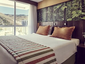 Habitación de hotel con una cama grande, dos almohadas, vista a la ciudad y un mural de un bosque en la pared.
