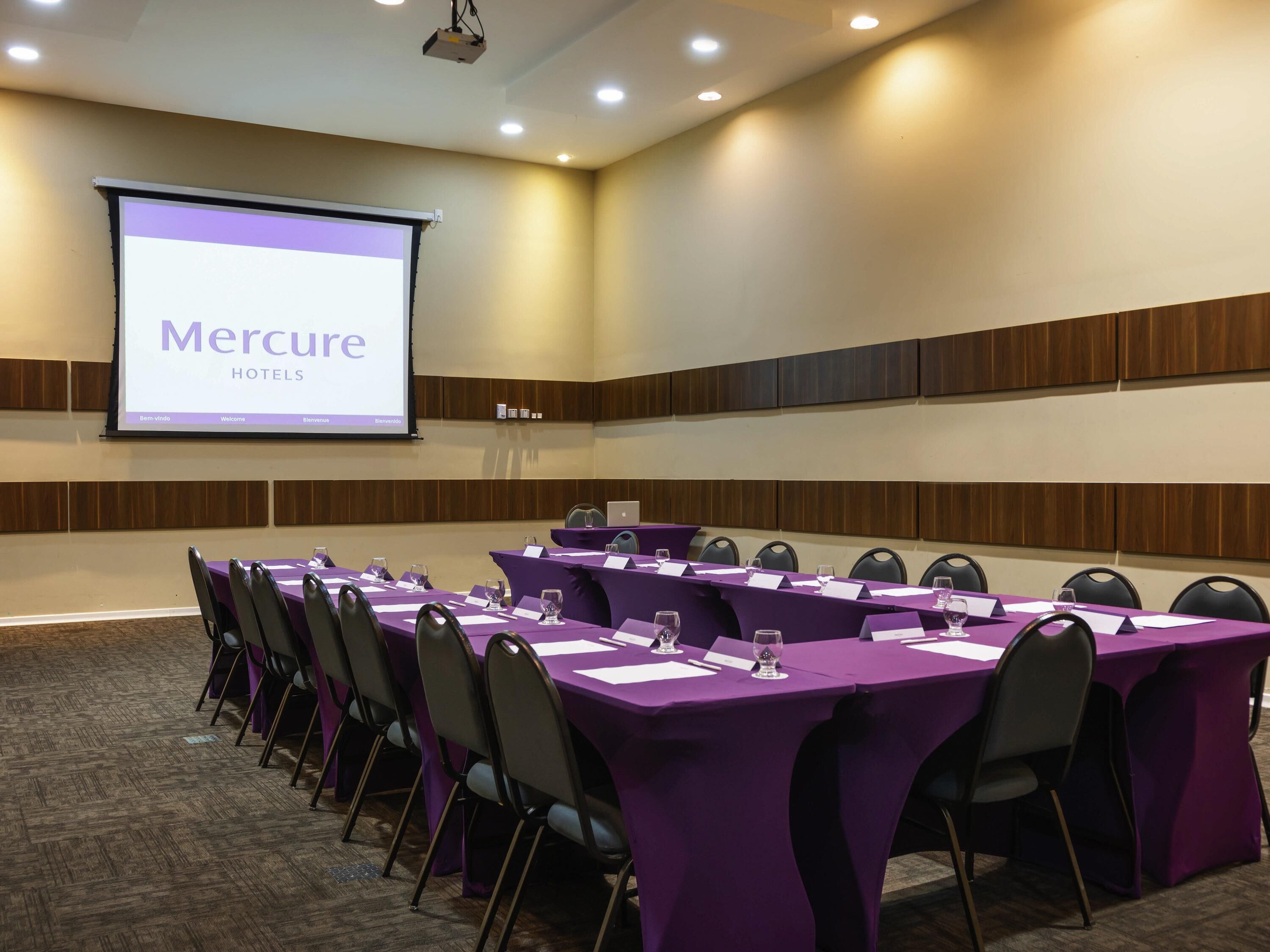 A conference room with a long table, chairs, and a presentation screen displaying 'Mercure HOTELS'.