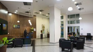 A modern reception area with a wooden reception desk, black seating, and a large potted plant. - Mercure RJ Nova Iguaçu Hotel (Nova Iguaçu)