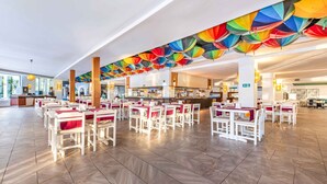 Ein großzügiges Restaurant mit weißen Tischen und Stühlen, einer langen Theke und bunten, hängenden Dekorationen.