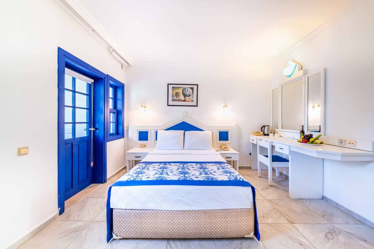 Ein Hotelzimmer mit Bett, Nachttischen, Schreibtisch, Stuhl, Spiegel und Tür.