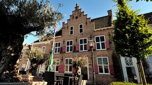 A traditional European building with a brick facade, multiple windows with shutters, and a small courtyard with outdoor seating. - Het Raedthuys Restaurant & Suites (Sint Maartensdijk)