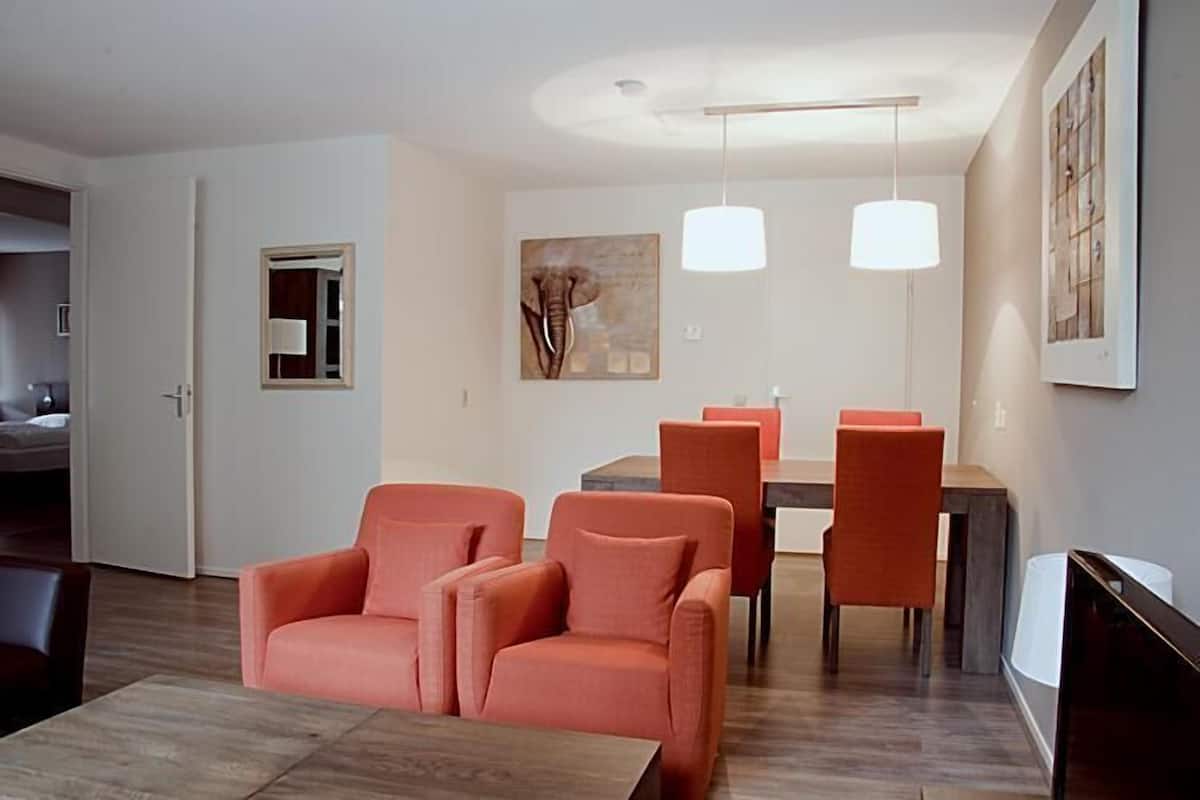 A modern living room with a sofa, chairs, a dining table, and pendant lights.