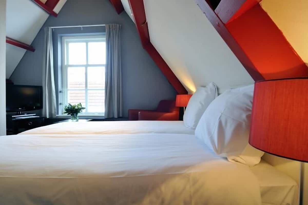 A bedroom with a large bed, a TV, and a window with curtains.