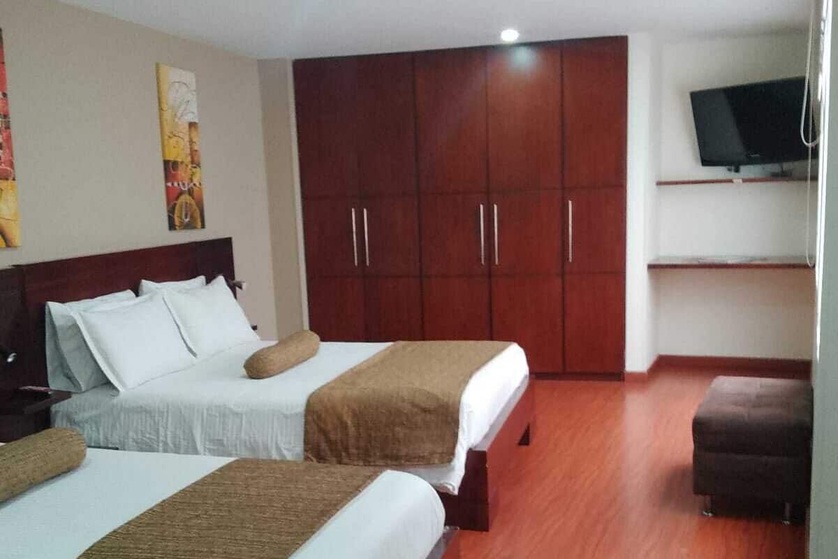 A hotel room with two beds, wooden wardrobe, and a TV on the wall.