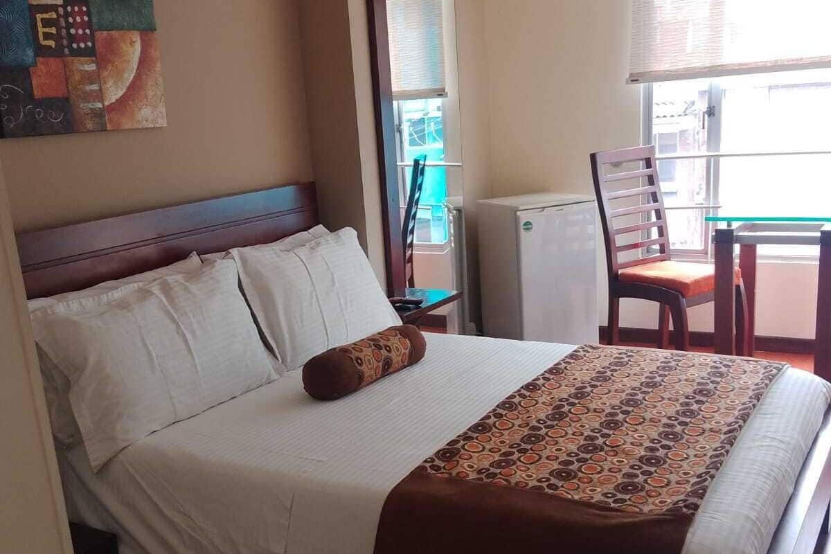 A hotel room with a bed, a chair, a table, and a window.