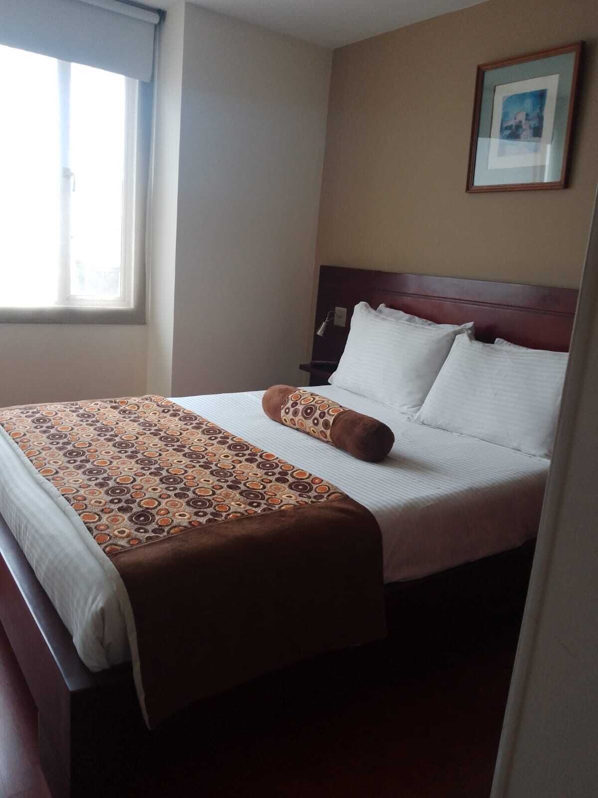 Ein Hotelzimmer mit einem großen Bett, einem Kopfteil, einem Nachttisch und einem Fenster.