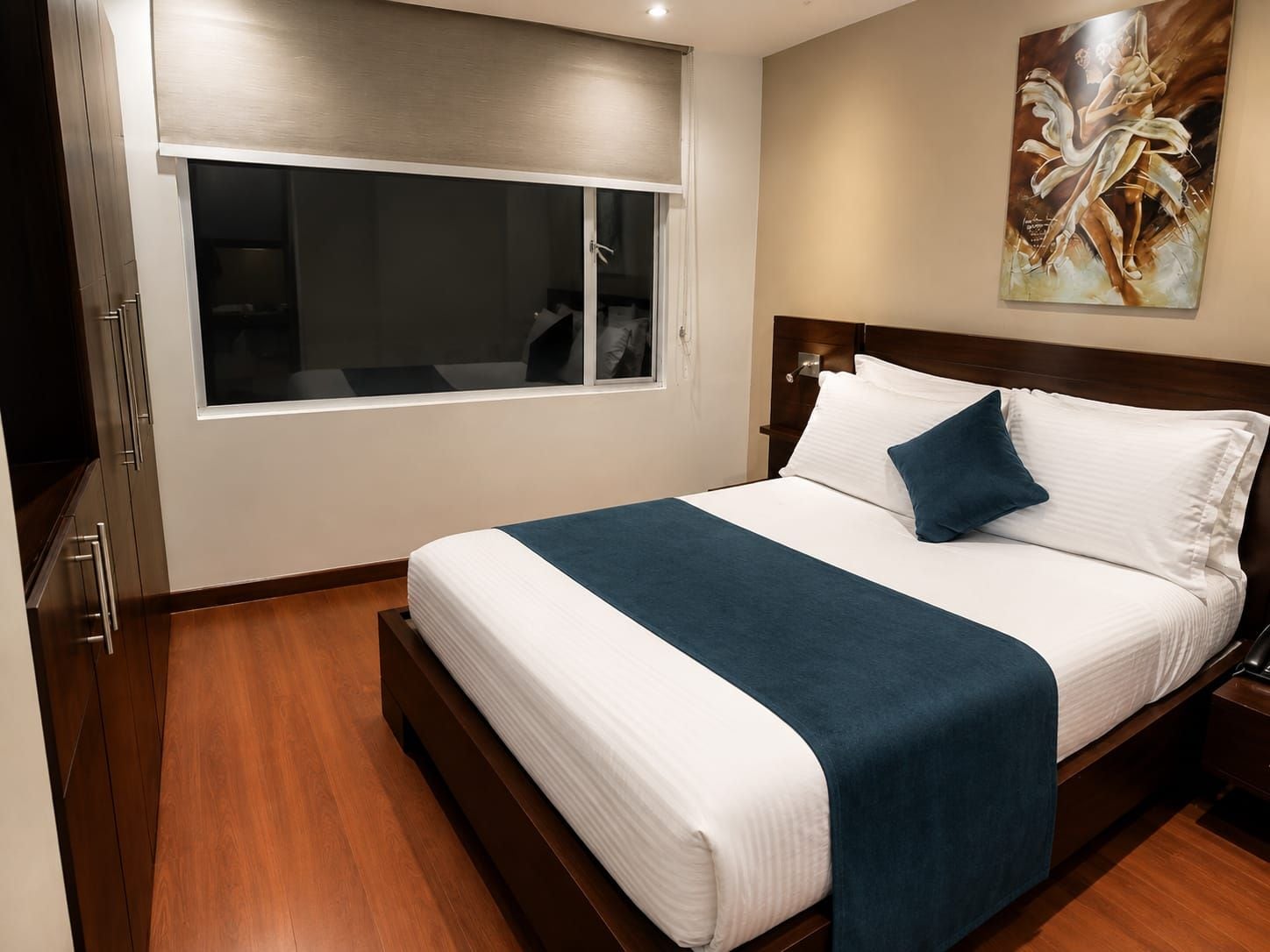 Una habitación de hotel con una cama grande, un ventanal, un cuadro en la pared y suelo de madera.