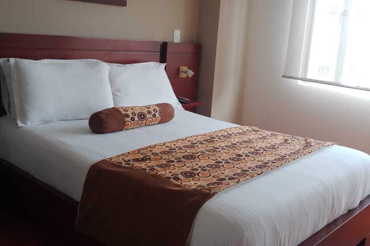 A neatly made bed with a patterned throw, a headboard, and a painting on the wall.