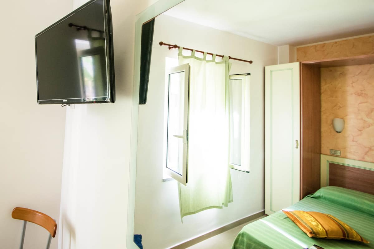 A room with a bed, a television mounted on the wall, and a window with curtains.