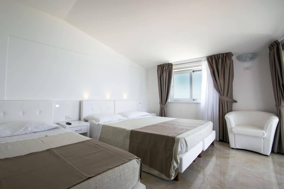 A hotel room with two beds, a white chair, and a window with curtains.