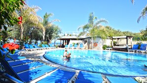 A swimming pool with blue lounge chairs, a lifeguard tower, and palm trees. - Resort Hotel Rocca di Vadaro (Ricadi)