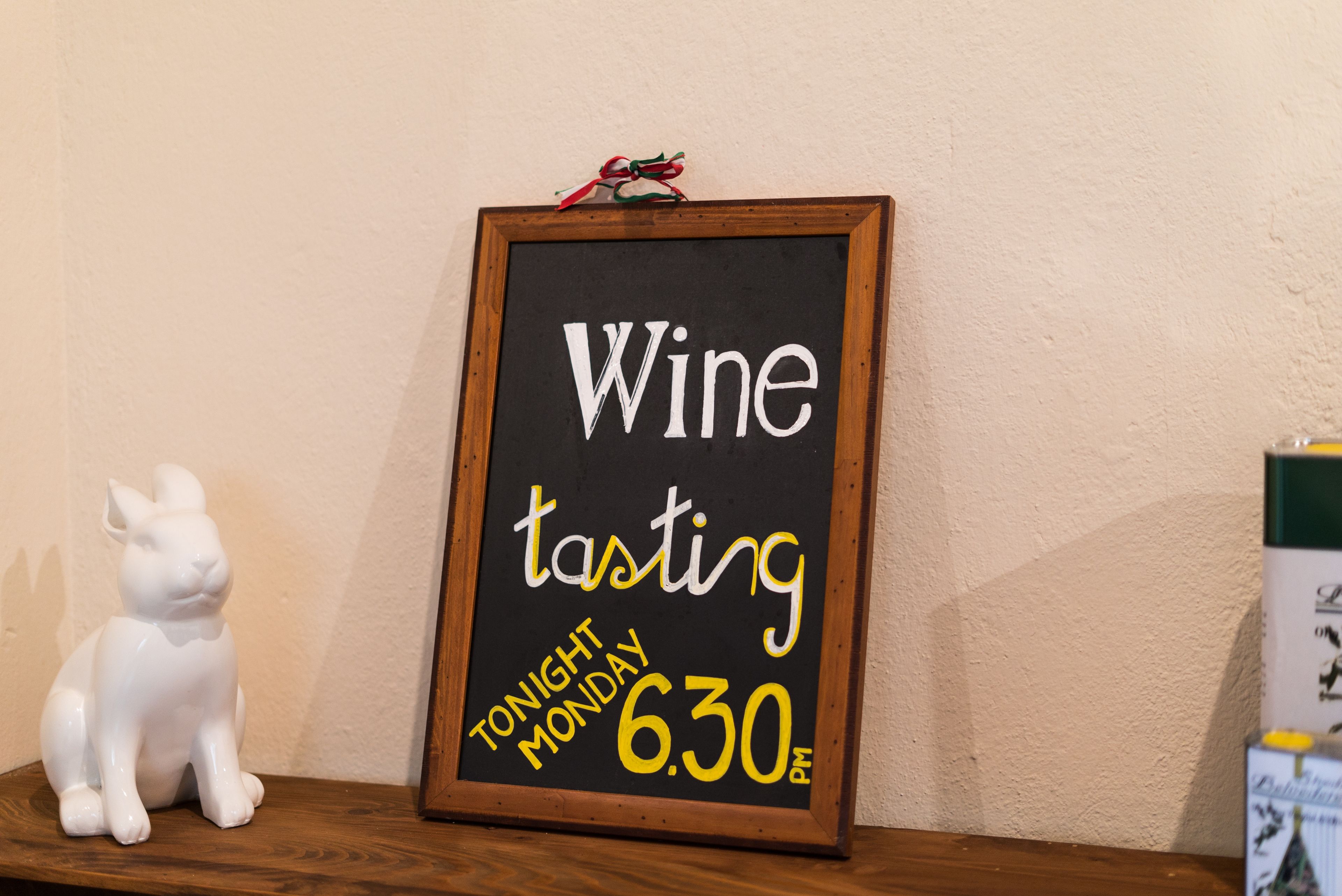 A sign for wine tasting on a blackboard with a wooden frame, a white ceramic rabbit, and a wooden shelf.
