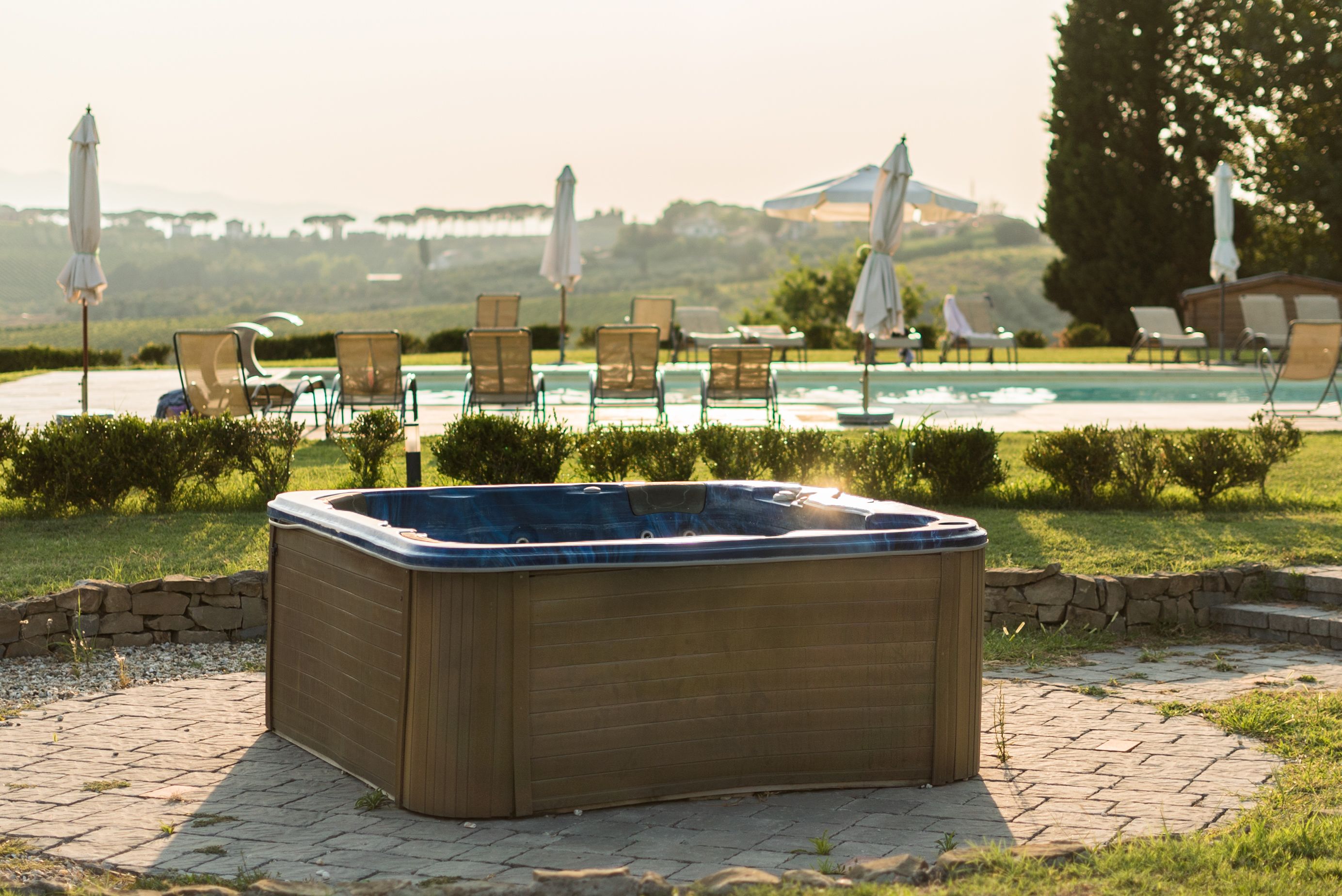 Un jacuzzi en un área exterior ajardinada, con sillones de descanso y sombrillas.