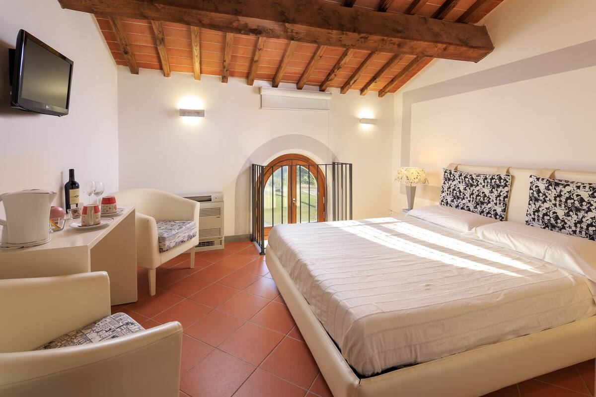 Un dormitorio con cama, un escritorio con silla, televisión y ventana con vistas a follaje.