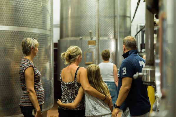Un grupo de personas en un entorno industrial metálico, posiblemente una cervecería o destilería, con tanques cilíndricos grandes y superficies de acero inoxidable.
