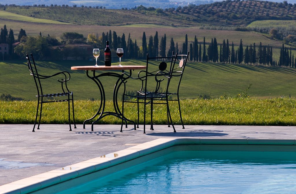 A poolside setting with a table and chairs, a bottle of wine, and a glass of wine.