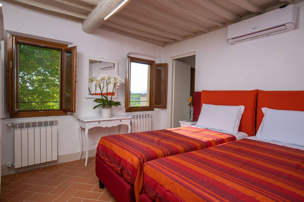 Un dormitorio con dos camas, una ventana con vistas, un radiador y un aparador blanco.