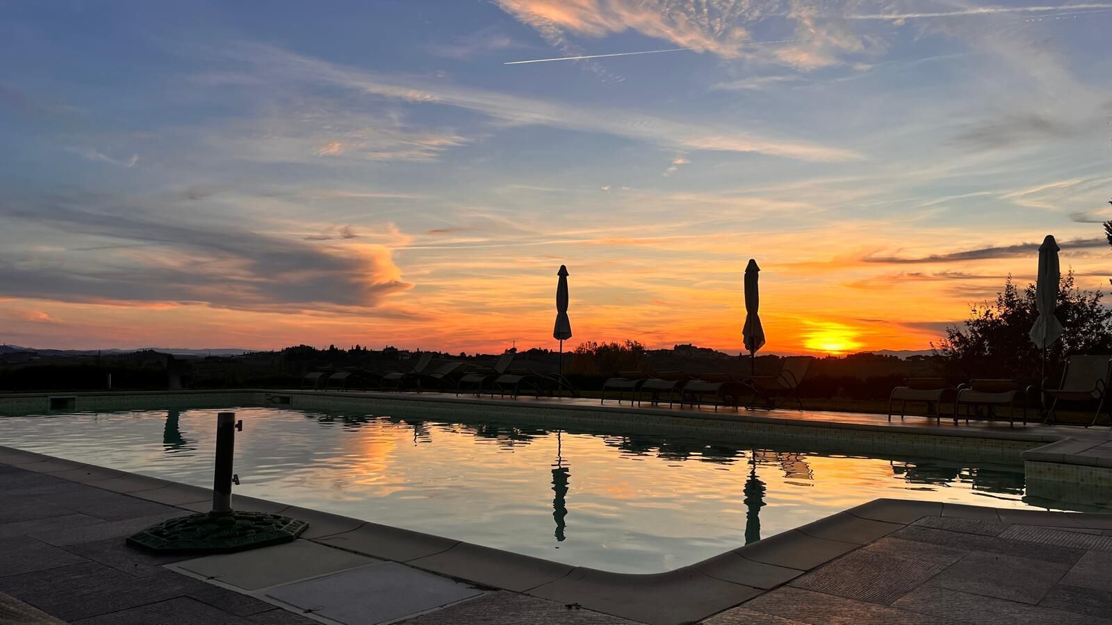 Piscina con sillones y sombrillas, frente a un cielo al atardecer.