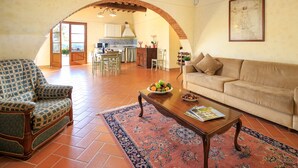 Amplia sala de estar con sofá, sillón y mesa de centro, comunicada con una cocina mediante un arco.