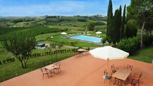 Un patio con piscina, mobiliario exterior y una vista panorámica de colinas onduladas y un pueblo lejano.